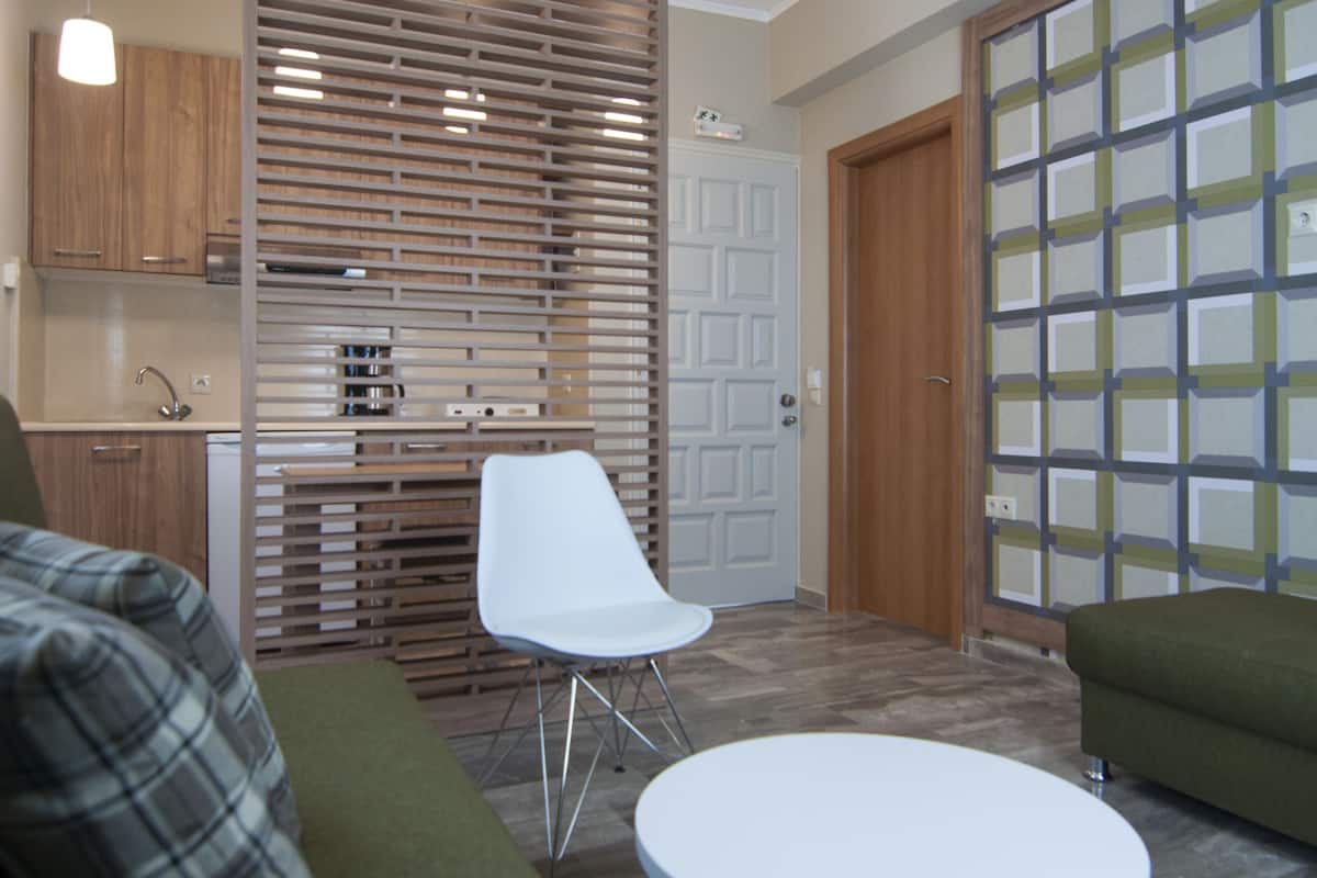 Una sala de estar moderna con un sofá verde, una mesa blanca y una silla blanca. Hay una zona de cocina con armarios de madera y una estufa empotrada.