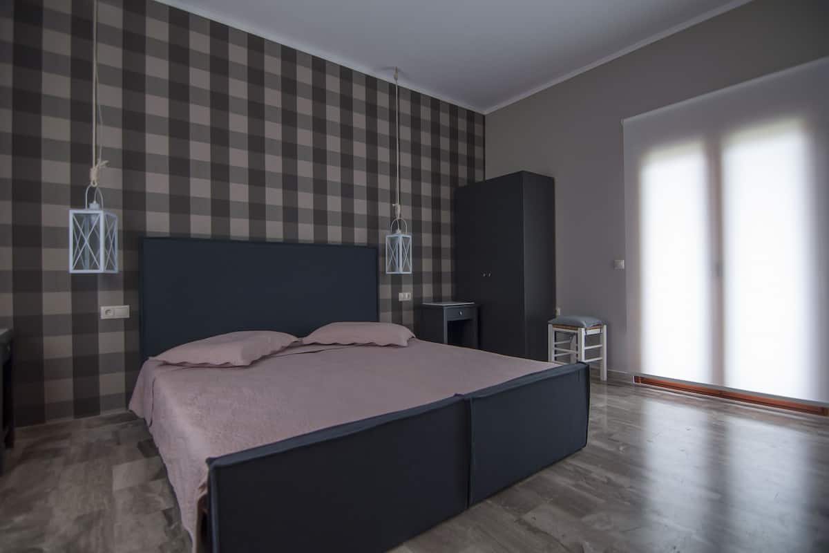 Un dormitorio con pared a cuadros, una cama con cabecero oscuro, una mesita de noche y un armario.