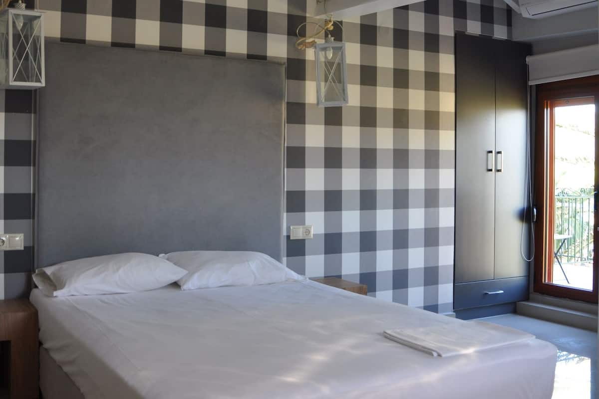 Un dormitorio con un estampado de cuadros en la pared, una cama con ropa de cama blanca y una estructura de techo de madera.