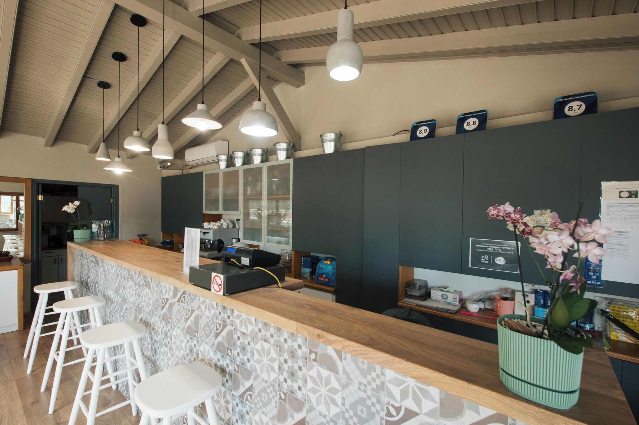 A reception area with a wooden counter, white bar stools, a potted orchid, and a wall-mounted sign.
