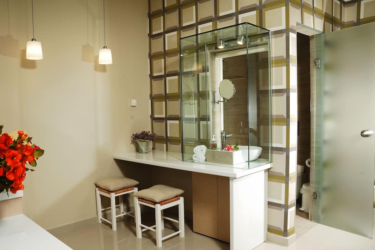 Un baño moderno con un lavamanos con recinto de vidrio, dos taburetes y un jarrón con flores.