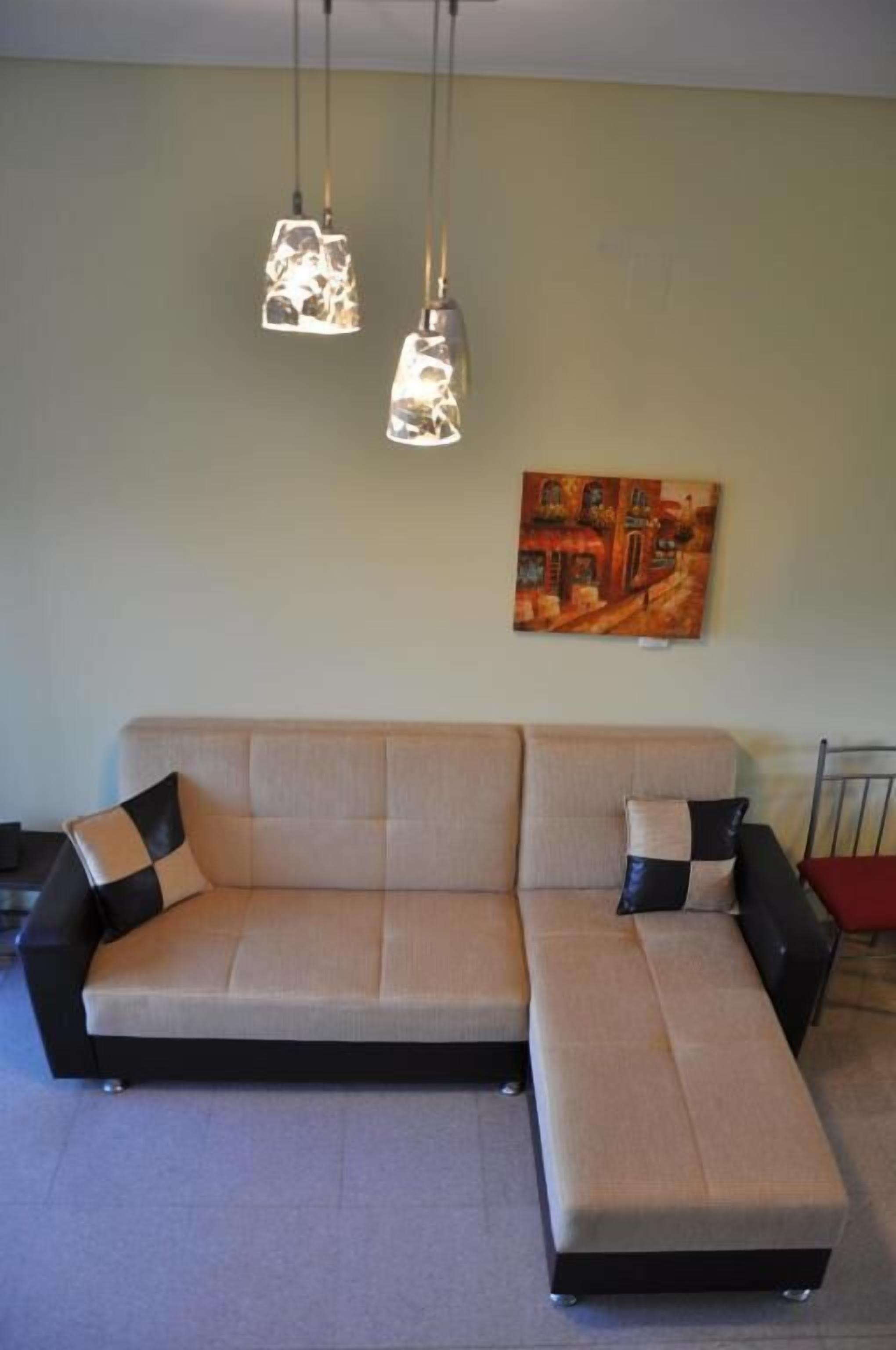Ein Ecksofa mit heller Stoffbezug, zwei Kissen in Schwarz und Beige sowie ein Gemälde an der Wand.