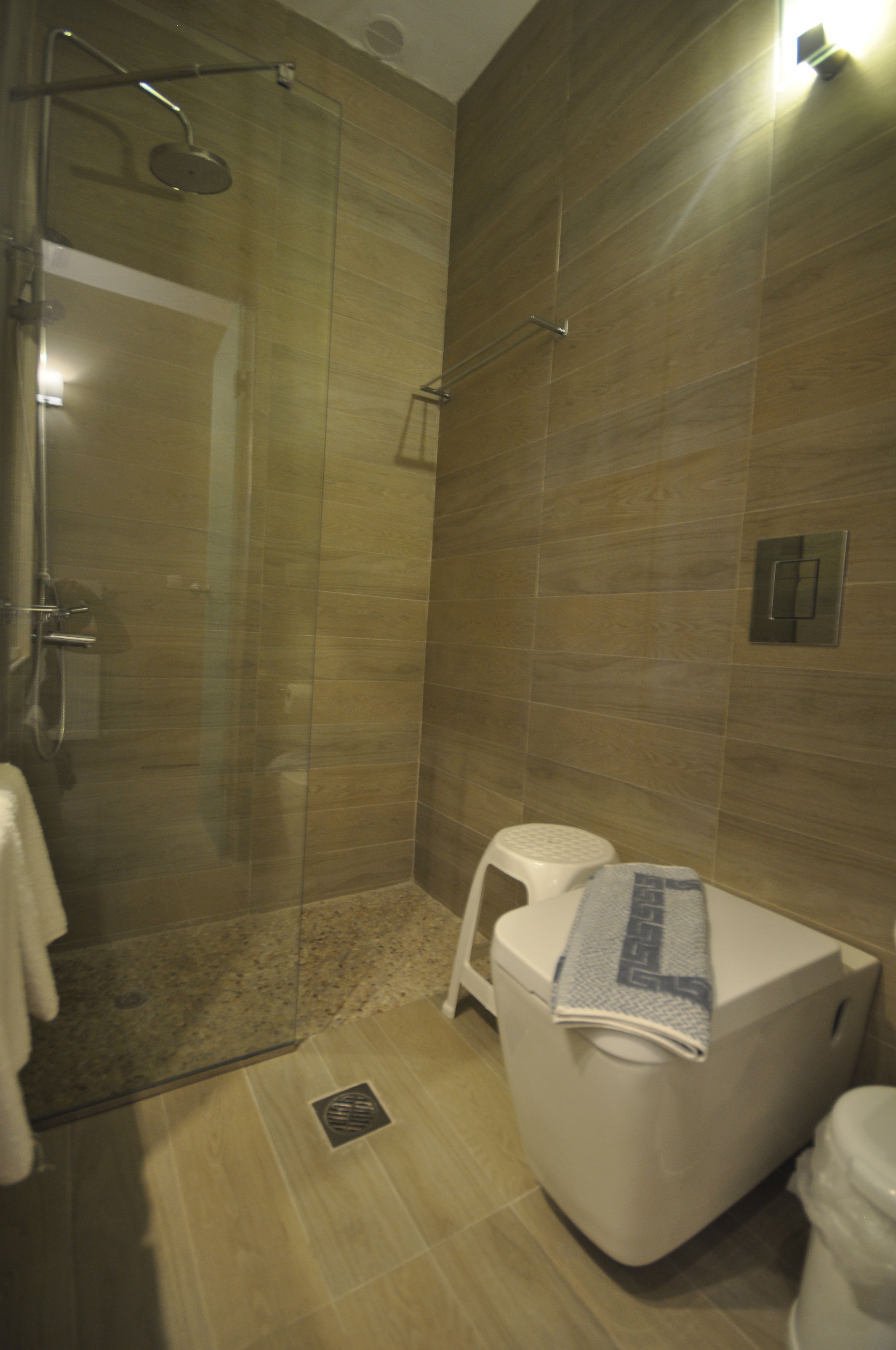 Un baño con ducha de vidrio, inodoro blanco y una toalla en el suelo.