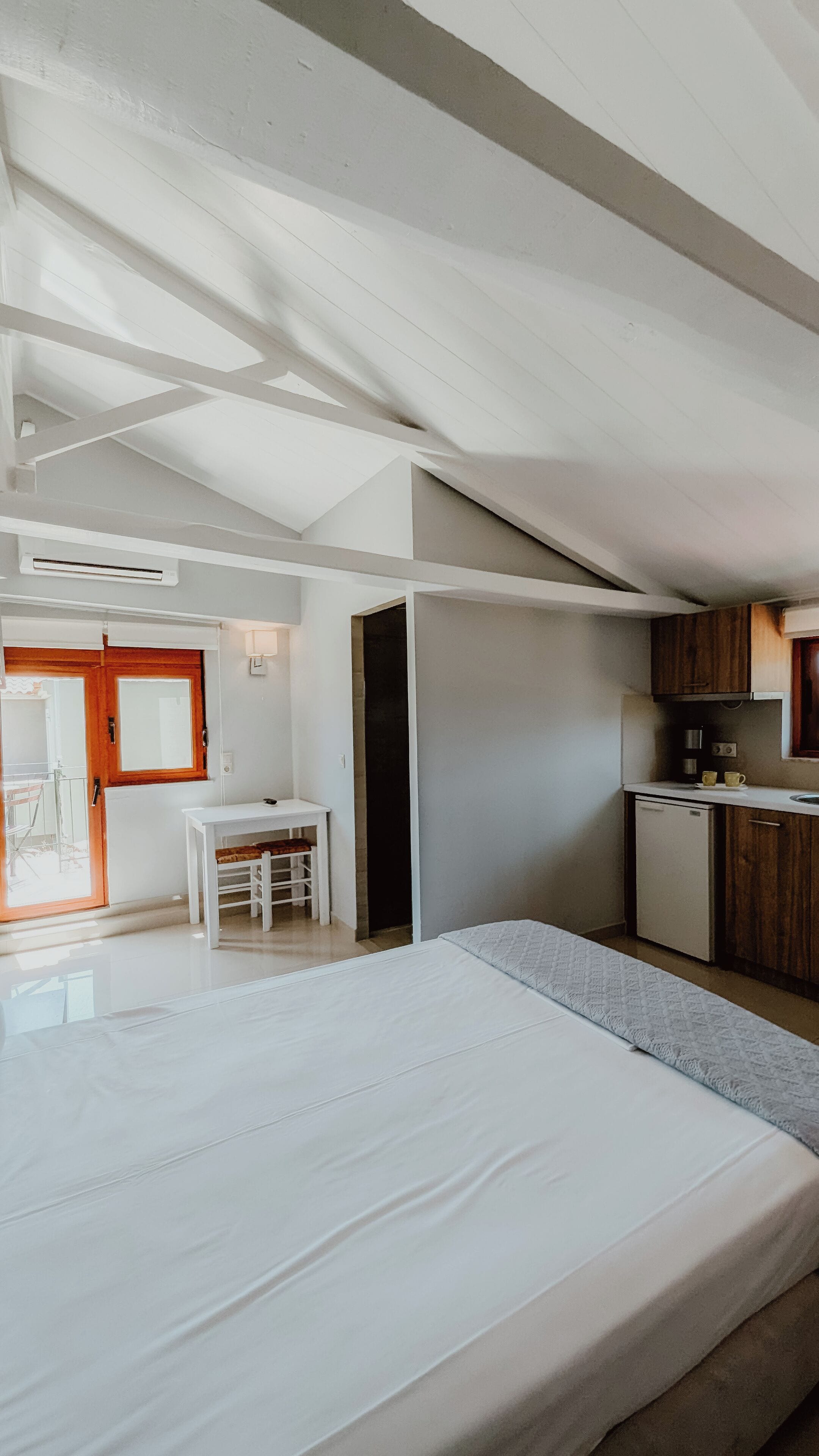 A modern bedroom with a large bed, a small desk, and a kitchenette.