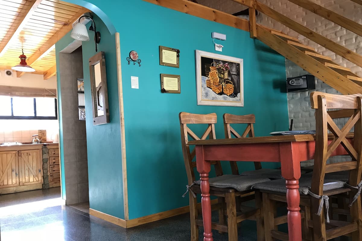 Zona pranzo con parete verde acqua, sedie di legno, tavolo rosso e un quadro incorniciato.