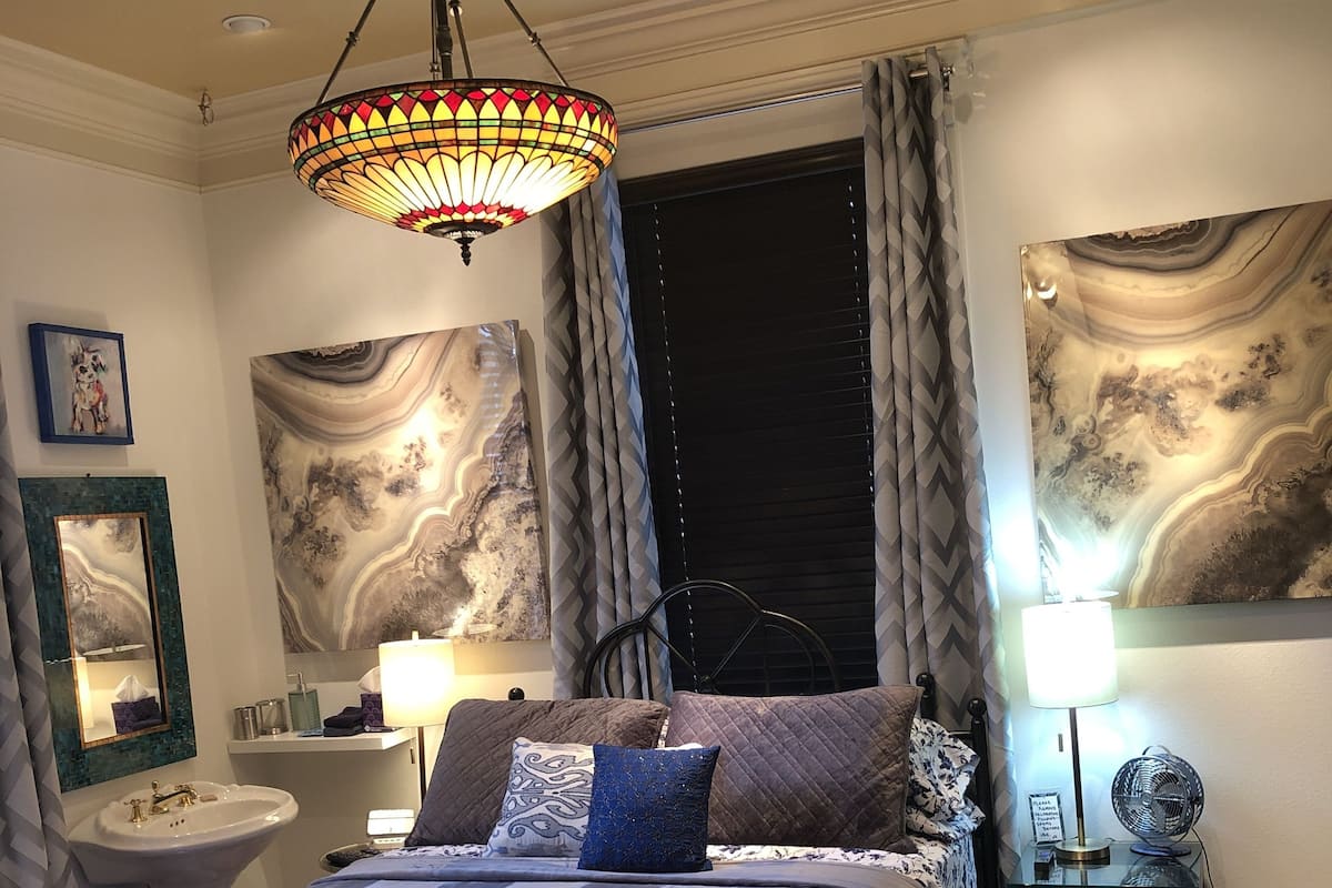 A bedroom with a bed, bedside table, lamp, and artwork on the walls.