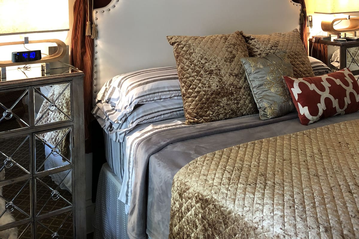 A bedroom with a four-poster bed, a clock on a bedside table, and a wall-mounted lamp.
