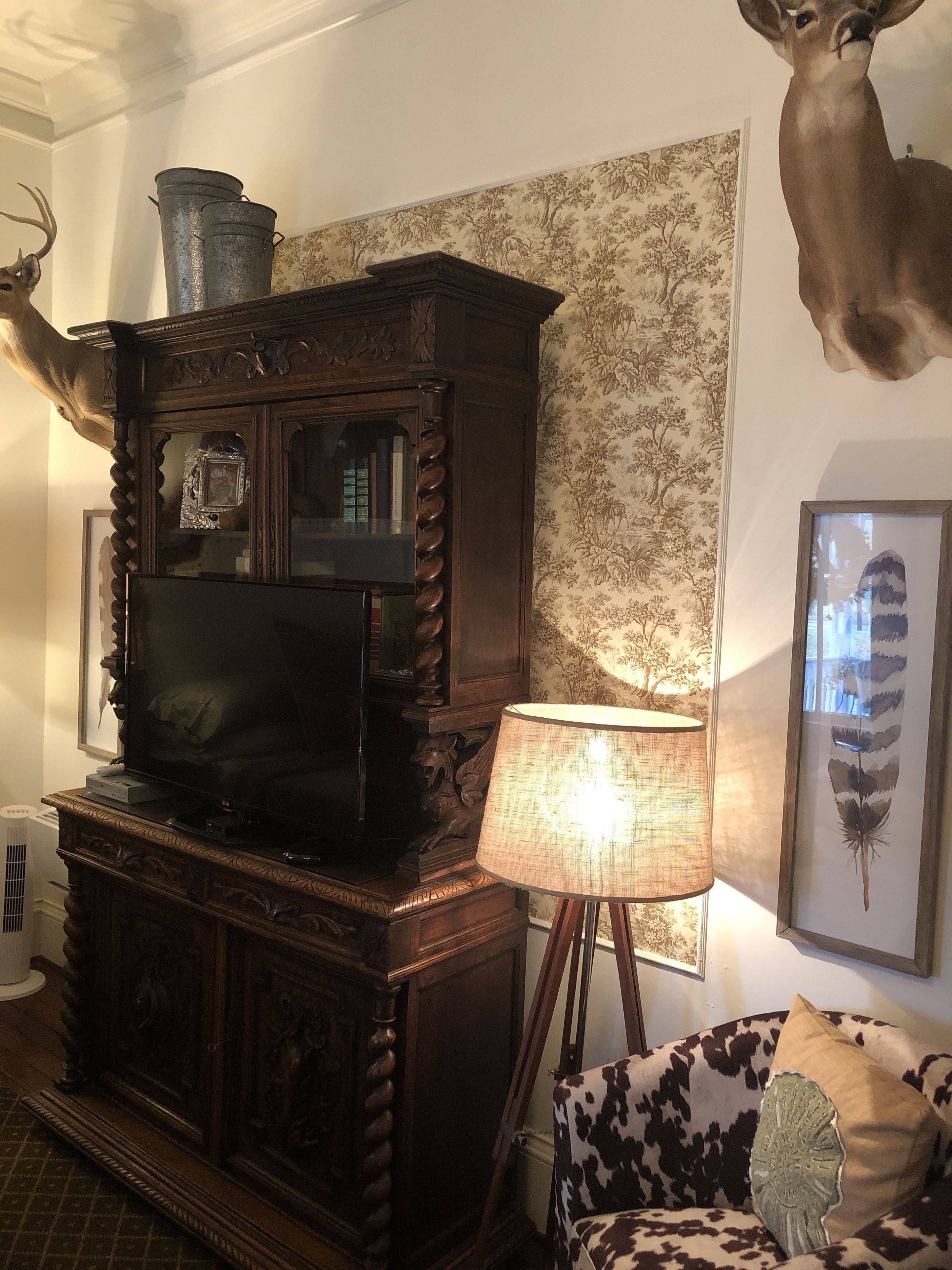 Un salon avec un meuble de rangement en bois pour les appareils multimédias, une tête de cerf accrochée au mur, une estampe botanique encadrée et un canapé à motifs.