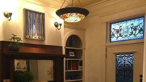 Una entrada cálidamente iluminada con chimenea, estanterías, un espejo decorativo y un ventanal de vidrio emplomado.