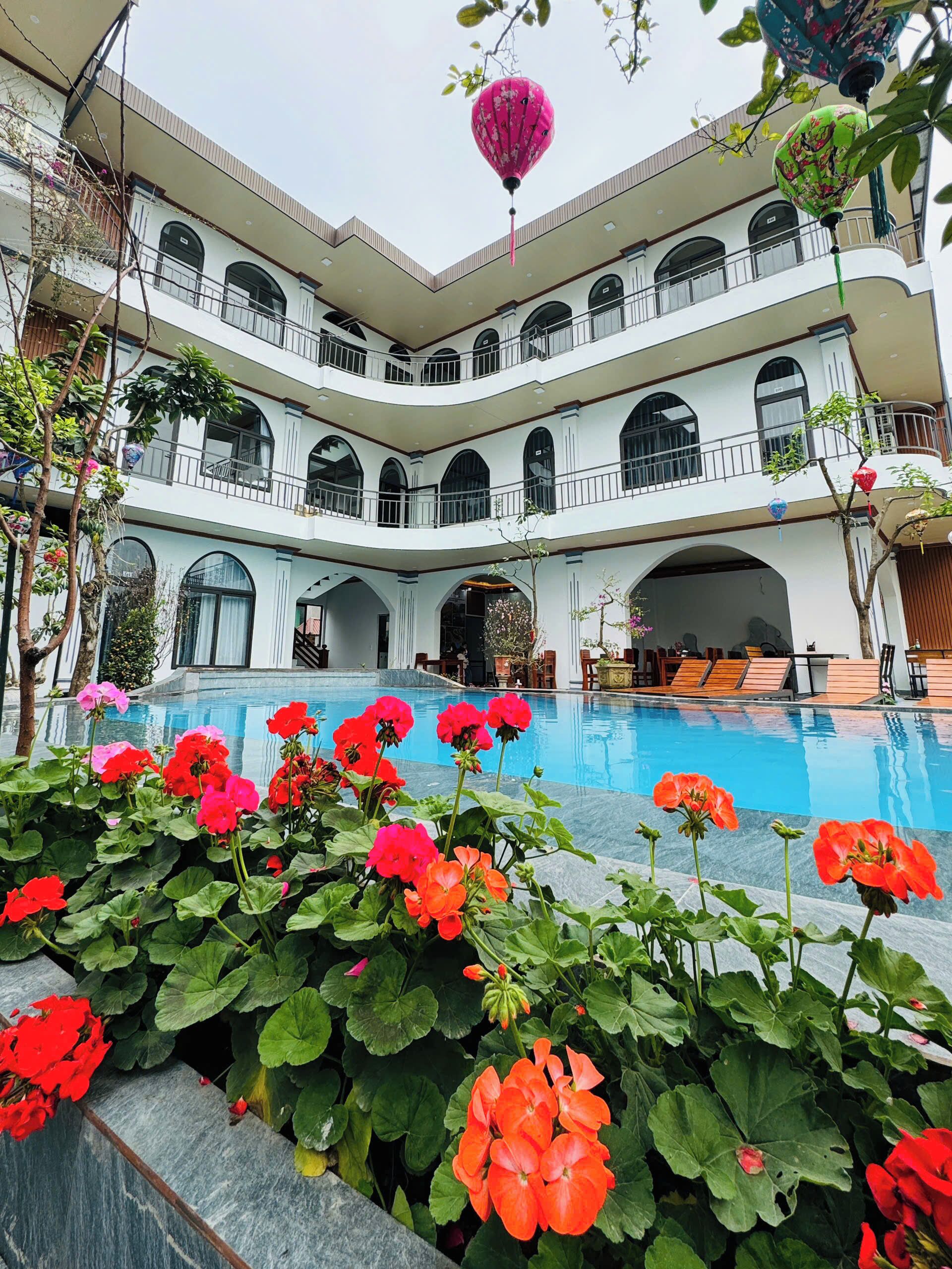 A multi-level hotel with a swimming pool and red flowers in the foreground.
