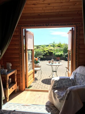 A wooden cabin with an open door leading to a patio area with a table, chairs, and potted plants. - Balnabrechan Lodge (Arbroath)
