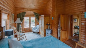 A log cabin room with a bed, rocking chair, dresser, and a small table with a vase of flowers. - Balnabrechan Lodge (Arbroath)
