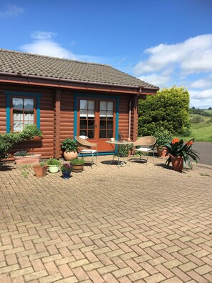 A log cabin with a tiled roof, a porch with wicker chairs, and potted plants. - Balnabrechan Lodge (Arbroath)