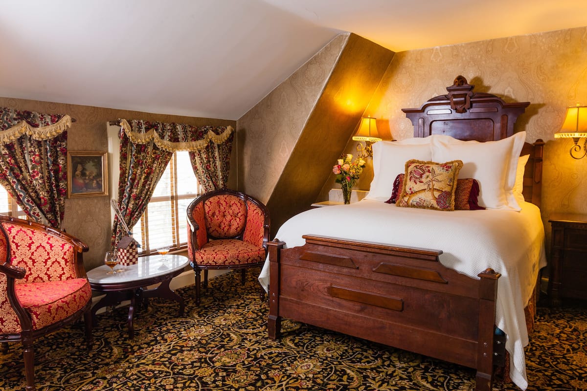 Un dormitorio con una cama grande, dos sillas, una mesita y una lámpara decorativa.