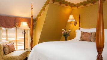 A bedroom with a large bed, a nightstand, a lamp, a chair, and a window with blinds.