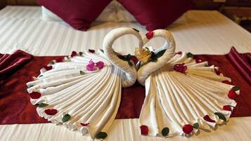 A bed with white linens, two red pillows, and a decorative swan made of towels with rose petals.