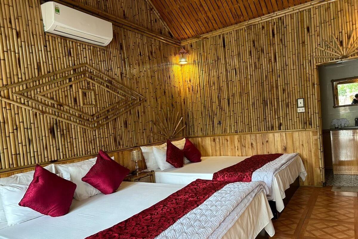 A room with two beds, each with white linens and red pillows, a bamboo wall, and a wooden ceiling.