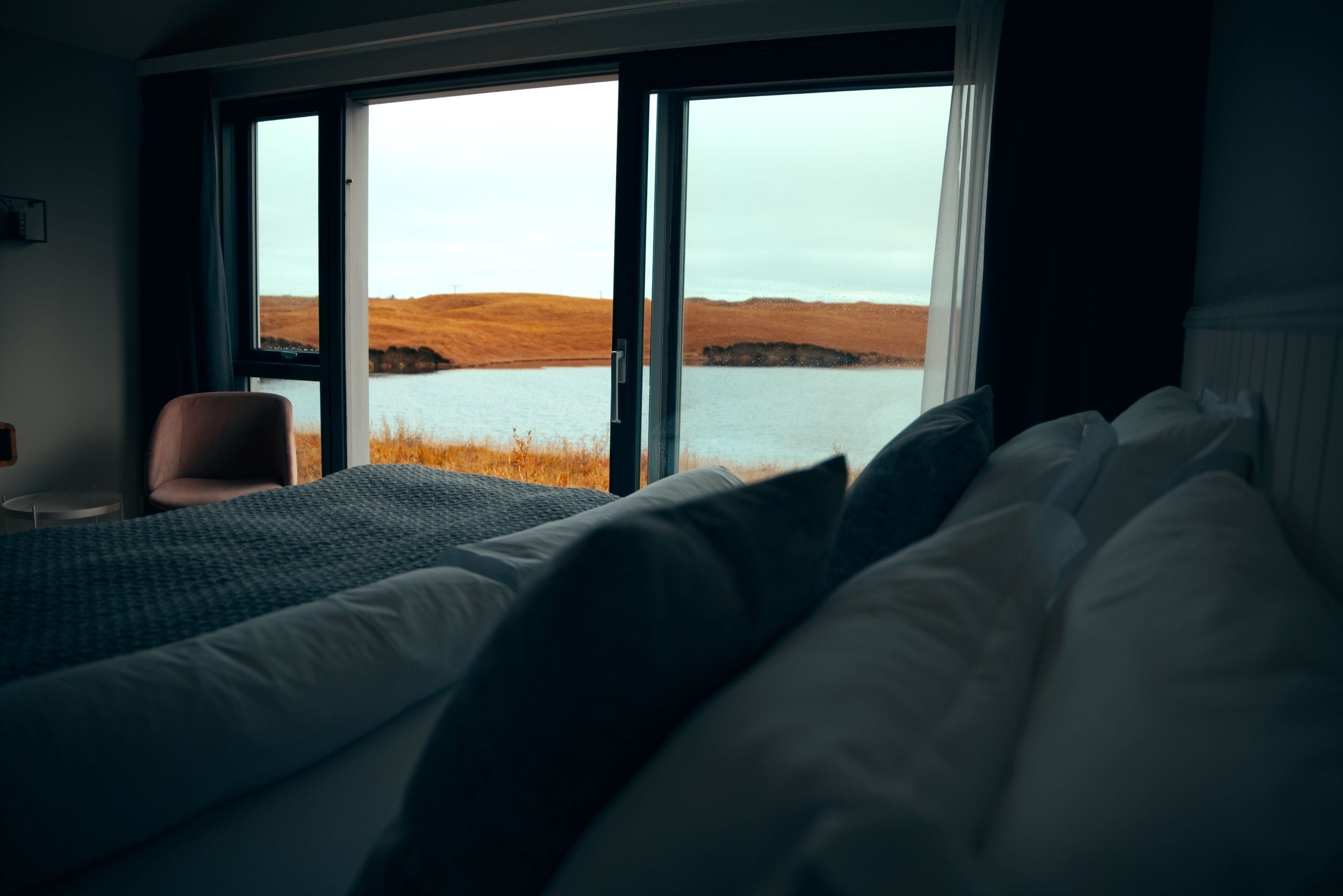 A bedroom with a large window, a bed with pillows, and a chair.