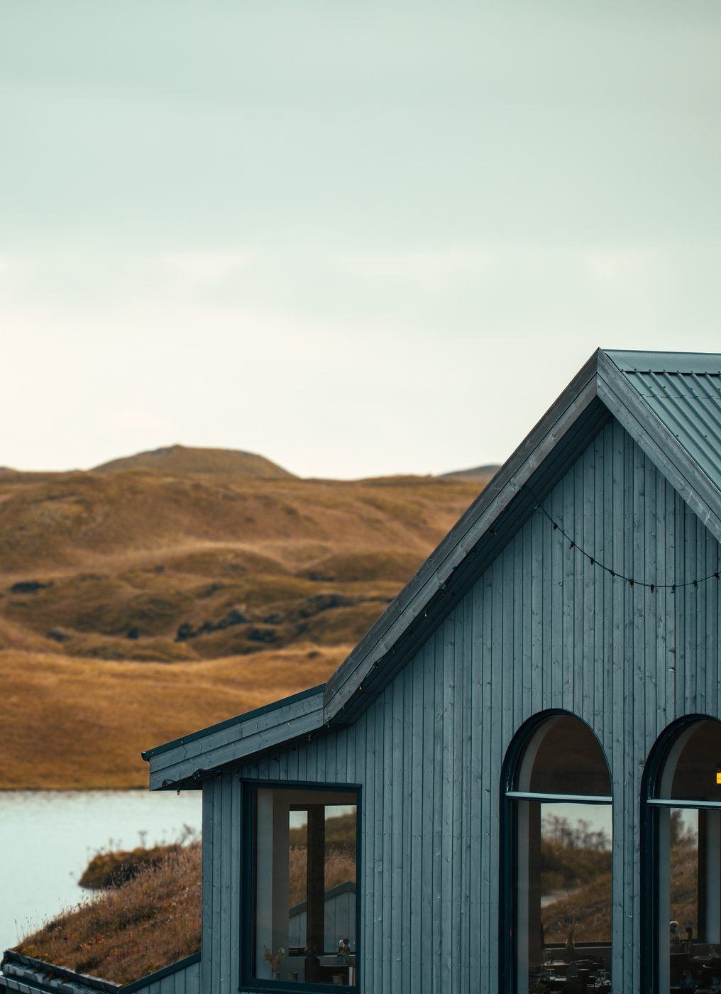 Un bâtiment en bois, doté d’un toit à pignon et de grandes fenêtres, qui se détache sur un paysage de collines et d’étendue d’eau.