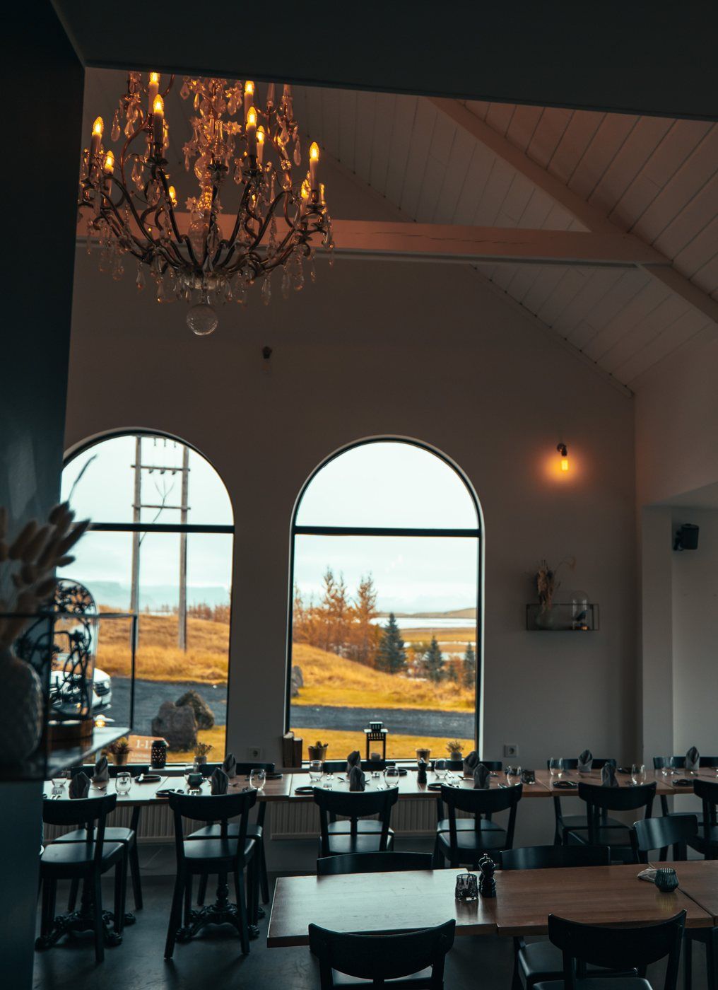 A dining area with a chandelier, large arched windows, and a view of a landscape.