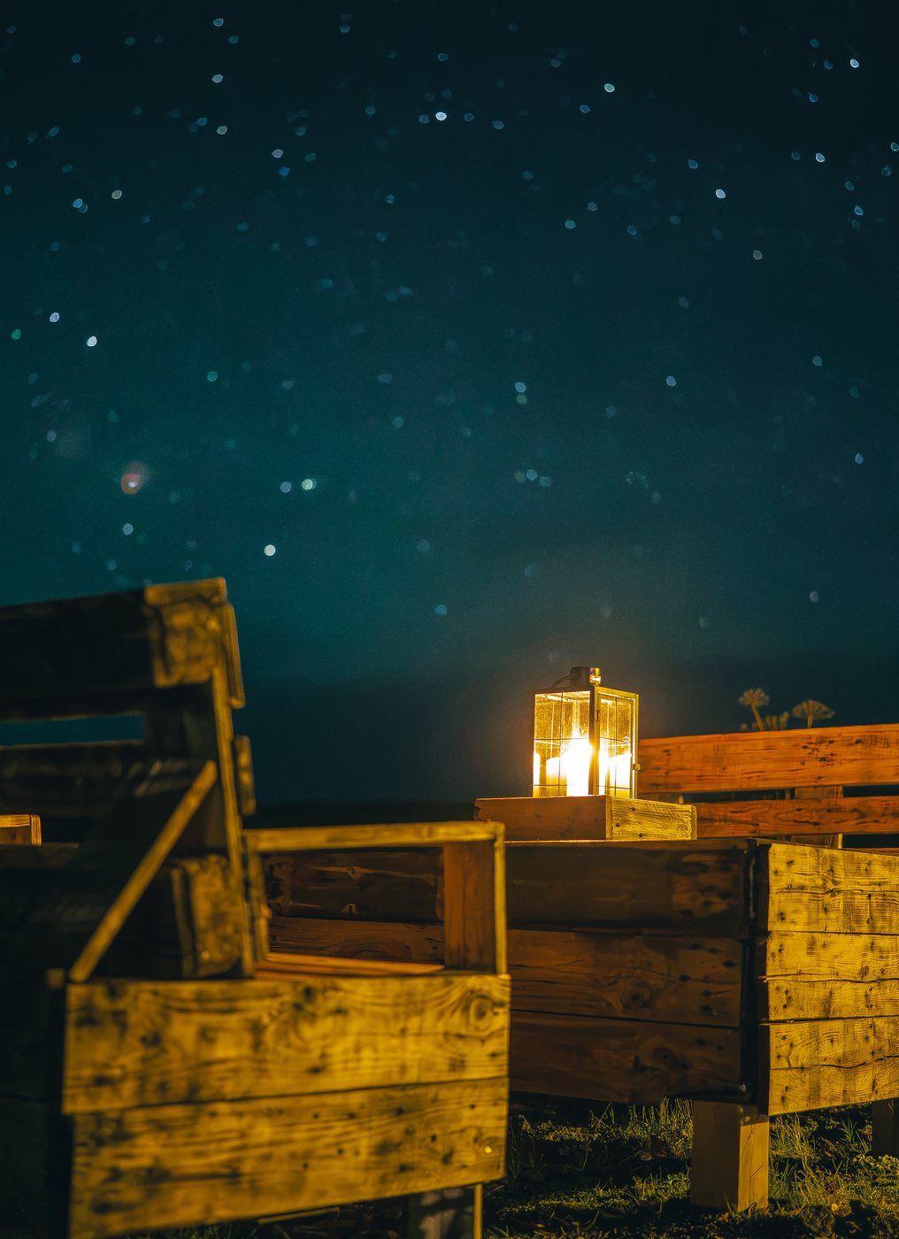 Une structure en bois, avec une lanterne allumée au centre, entourée d’un ciel nocturne sombre où l’on peut voir des étoiles.