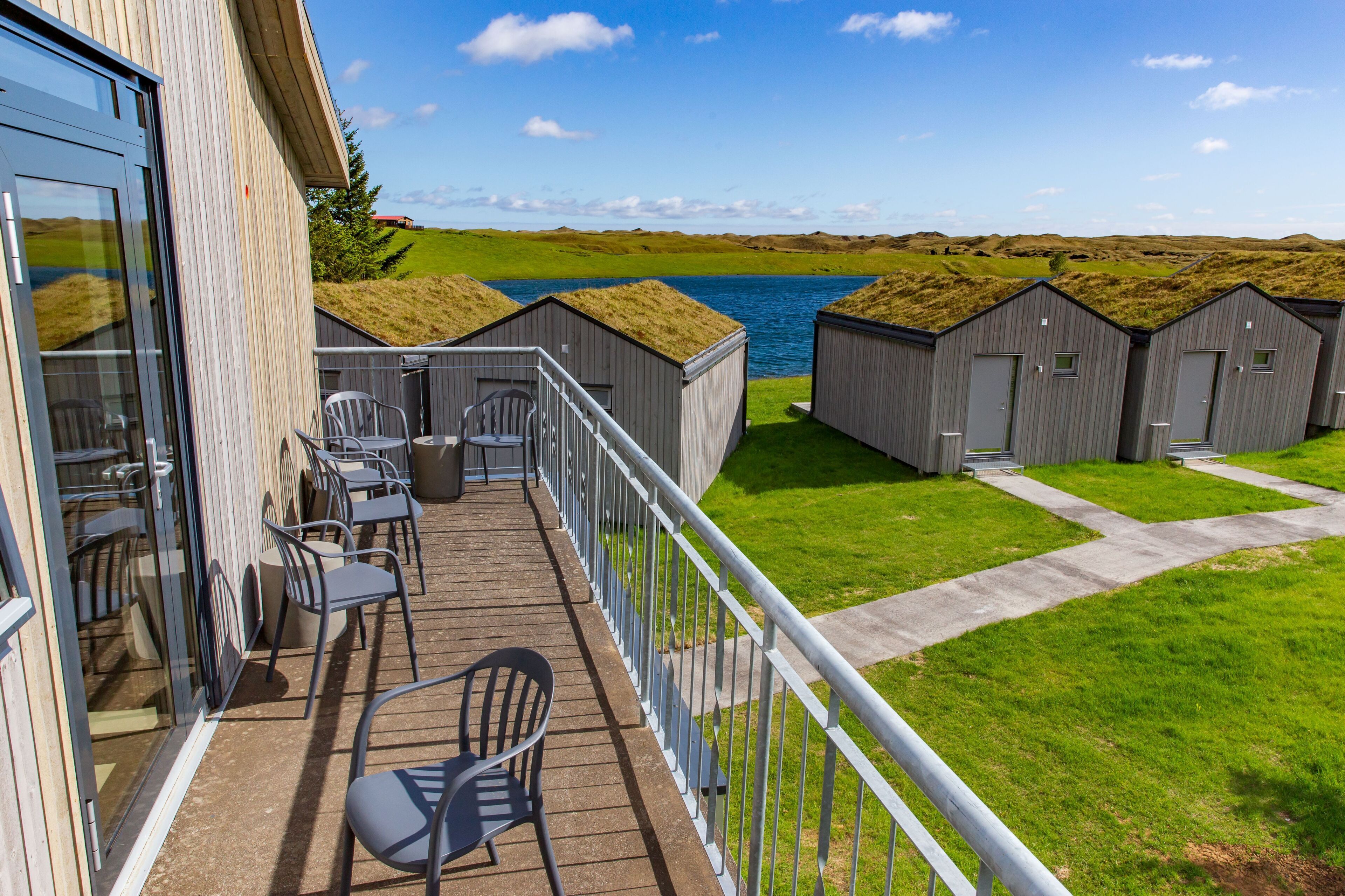 A balcony with outdoor seating and a view of a lake and grassy landscape.
