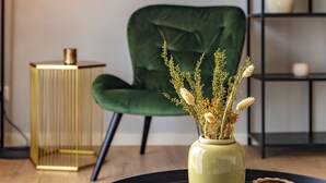 Una stanza con una poltrona rivestita in verde, un vaso con piante secche, un tavolino dorato e un vassoio nero.
