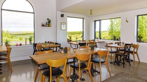 Un'ampia sala da pranzo con grandi finestre, tavoli e sedie in legno.