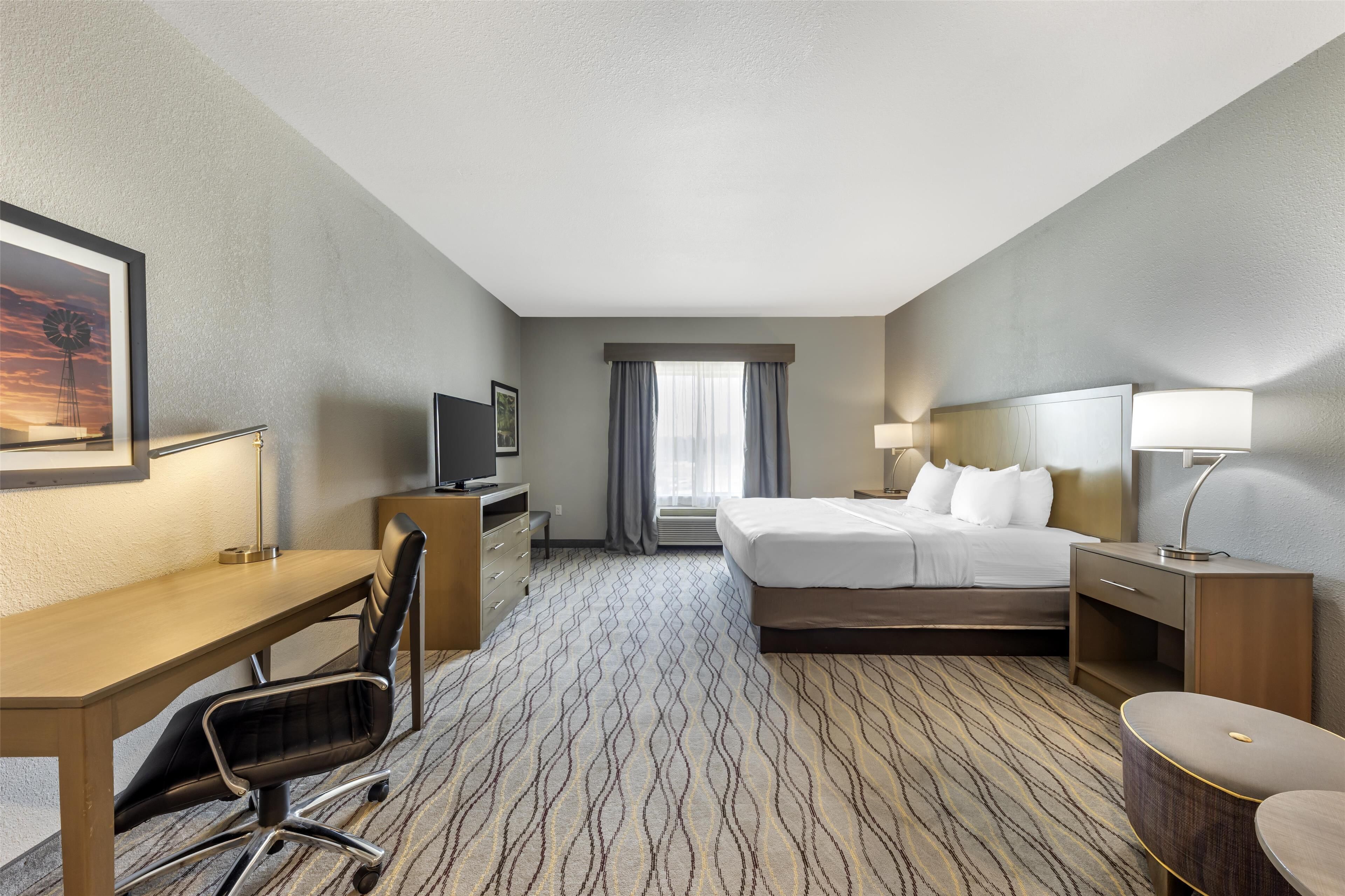 Une chambre d’hôtel équipée d’un lit, d’un bureau, d’une chaise, d’une télévision et d’une grande fenêtre avec des rideaux.