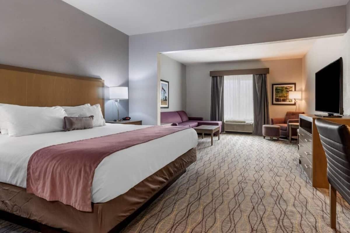 A hotel room with a large bed, a desk, a chair, a television, and a sofa.
