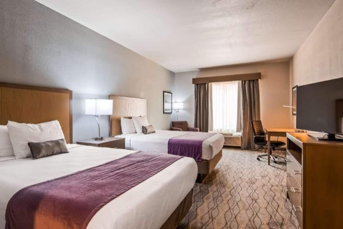 A hotel room with two beds, a desk, a chair, a television, and a window with curtains.