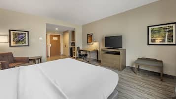 A hotel room with a large bed, a desk, a television, a chair, and a bench.