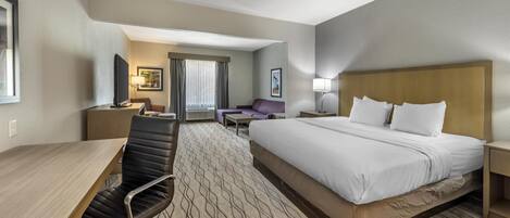 A hotel room with a large bed, a desk with a chair, a sofa, and a television.
