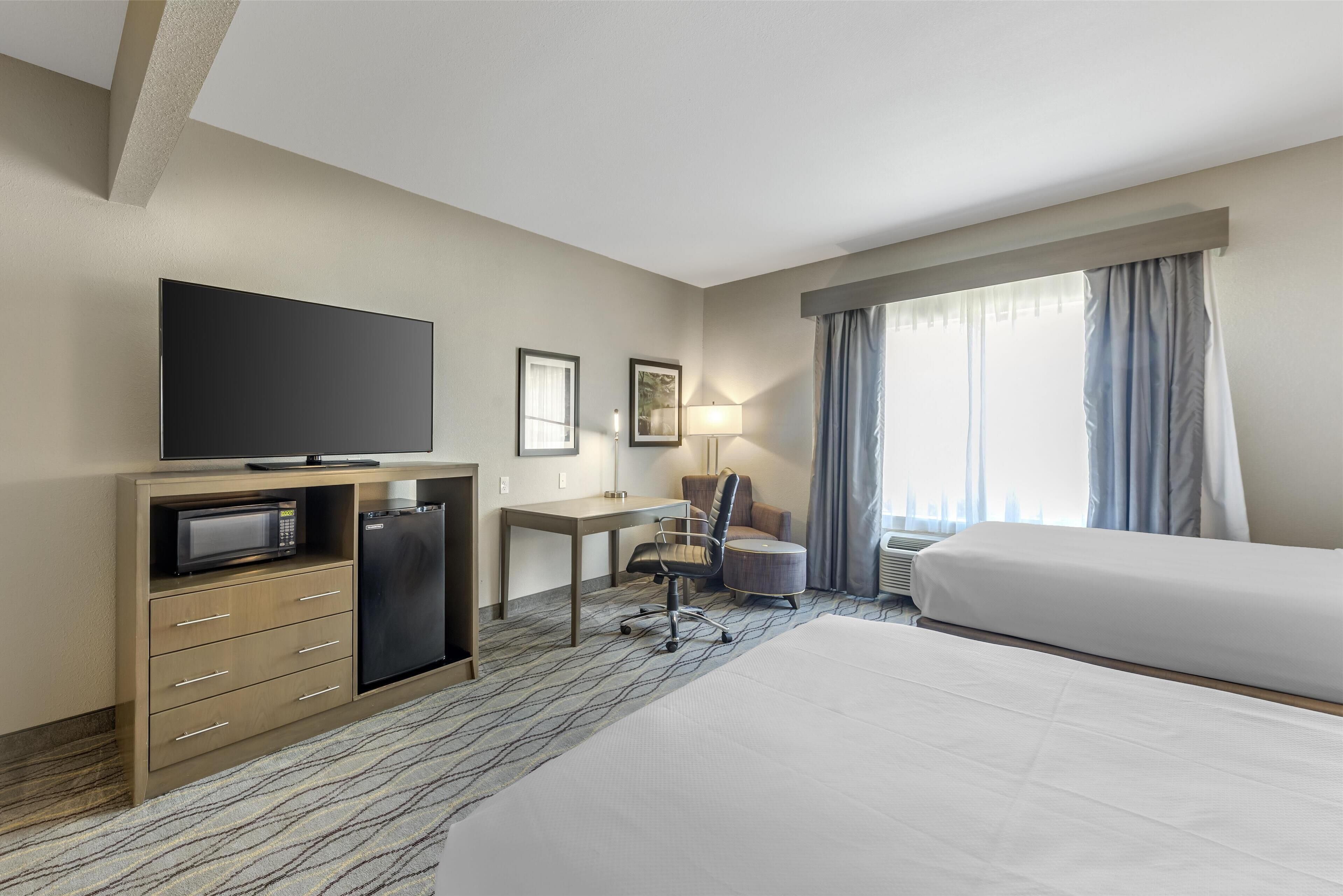 A hotel room with a bed, a desk with a chair, a television, a microwave, and a refrigerator.