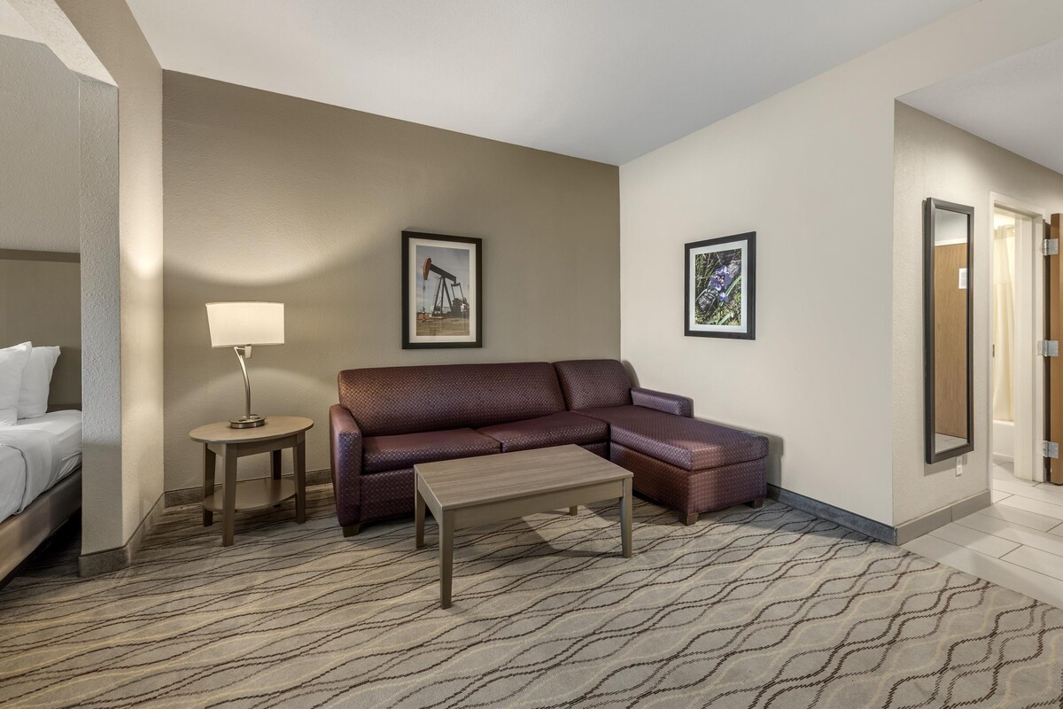 A hotel room with a bed, a sofa, a coffee table, a lamp, and two framed pictures on the wall.