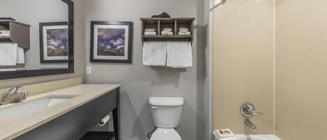 Une salle de bain moderne avec un lavabo, des toilettes et une baignoire. On y trouve des étagères avec des serviettes et un tableau encadré au mur.