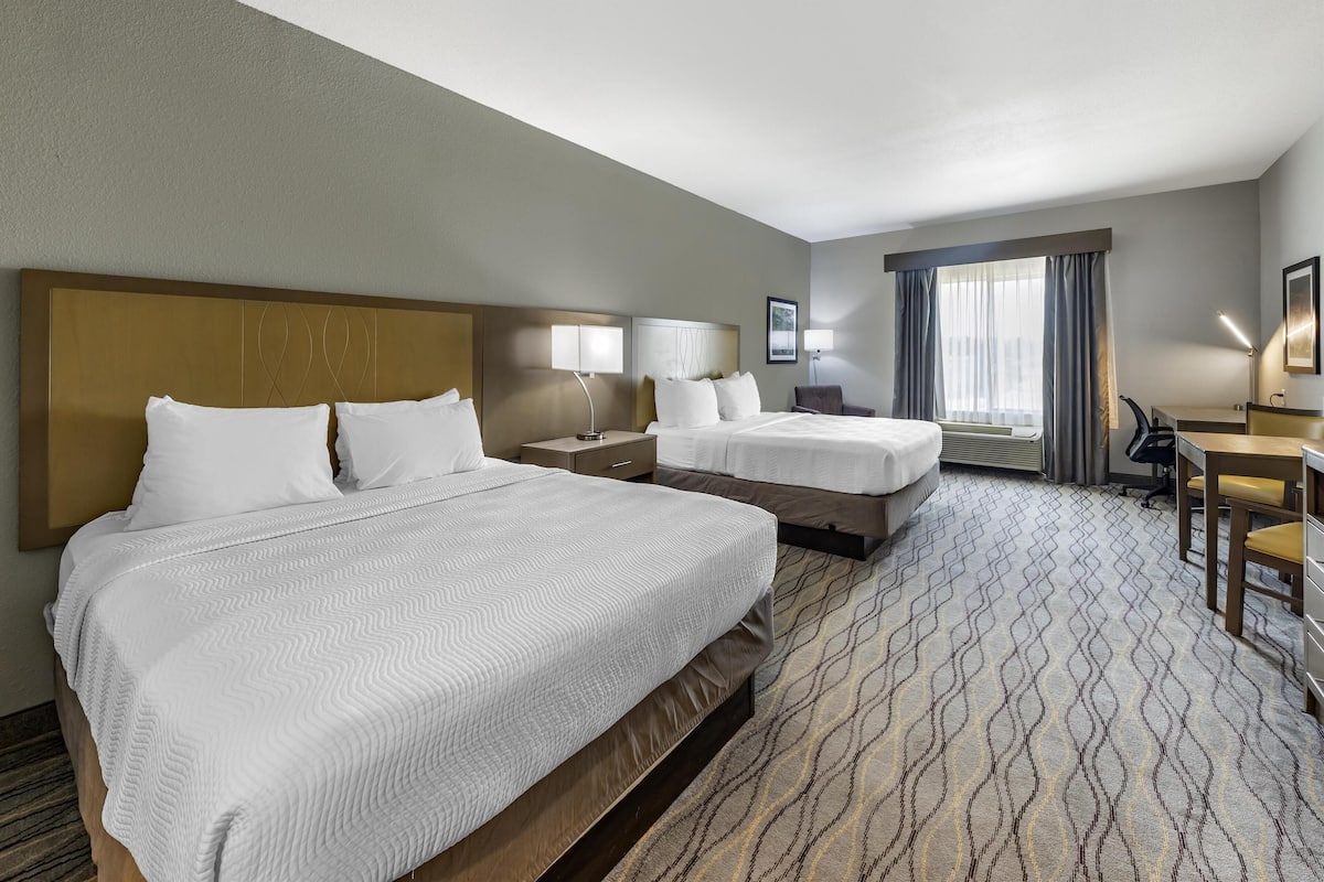 A hotel room with two beds, a desk, and a chair.