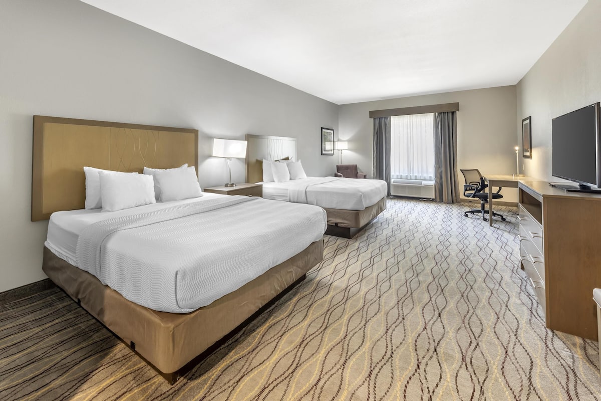 A hotel room with two beds, a desk, a chair, a TV, and a large window with curtains.