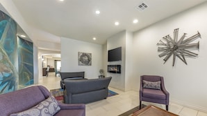 Un salon moderne comprenant un canapé, un fauteuil et une table basse, un téléviseur à écran plat fixé au mur, ainsi qu’un élément décoratif en métal.