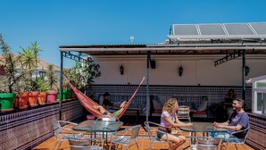 An outdoor patio with metal chairs and tables, a hammock, and potted plants. - Triana Backpackers (Seville)