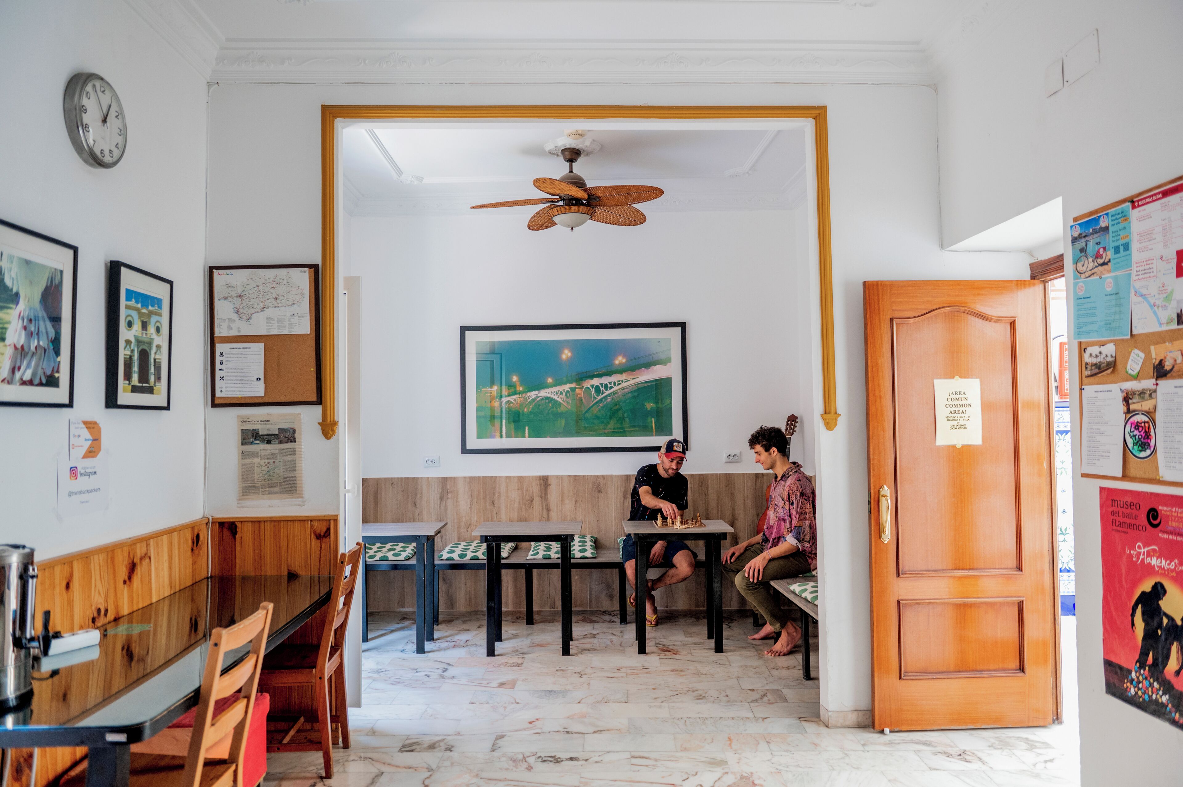 A room with a wooden bench, a table, a ceiling fan, and a door with a sign.