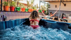 A person in a red swimsuit in a hot tub with a tiled patio and potted plants in the background. - Triana Backpackers (Seville)