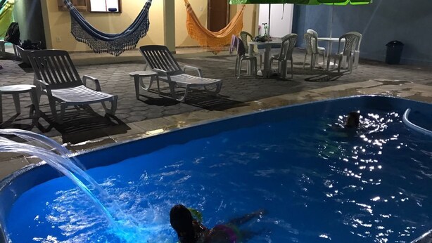 Una piscina con una persona nadando, rodeada de sillas de descanso y una hamaca.