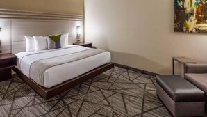 A hotel room with a large bed, a nightstand, a bedside table, a chair, and a painting on the wall. - Comfort Inn & Suites Houston I-45 North - IAH (Houston)