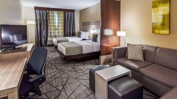 A hotel room with a bed, two bedside tables, a TV, a desk, a chair, a sofa, and a carpeted floor. - Comfort Inn & Suites Houston I-45 North - IAH (Houston)