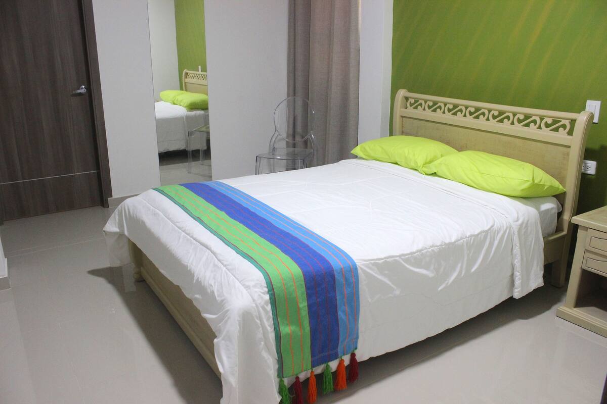 A neatly made bed with a colorful striped blanket, a wooden headboard, and a green pillow.