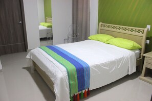 A neatly made bed with a colorful striped blanket, a wooden headboard, and a green pillow. - Hotel Emerawaa (Riohacha)