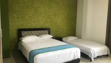 Habitación de hotel con dos camas, pared verde con textura y suelo blanco.