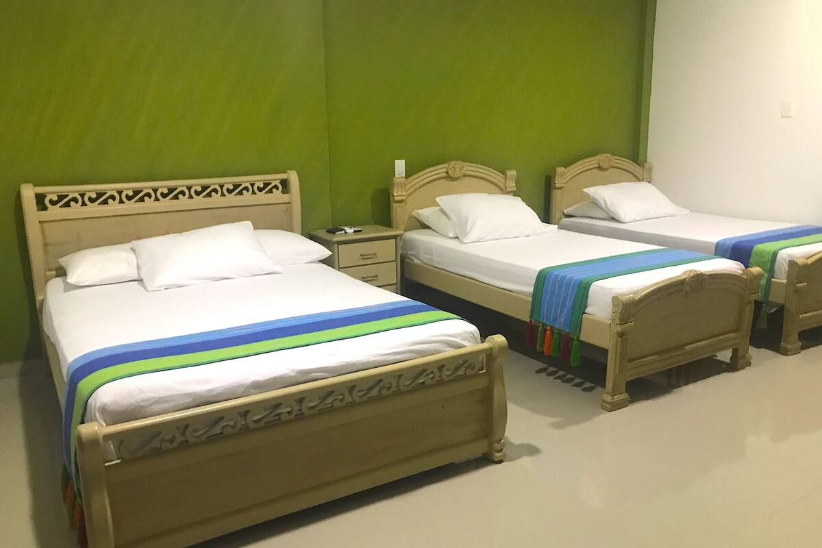 A hotel room with three wooden beds, each with white bedding and a colorful striped blanket.