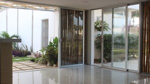 A modern interior with a glass door leading to a garden, a tiled floor, and a minimalist design. - Hotel Emerawaa (Riohacha)